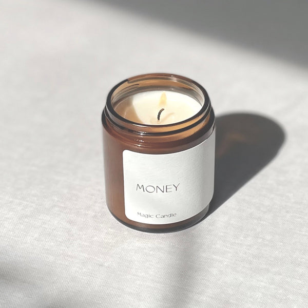 lit candle in amber colored jar labeled " money magic candle" 