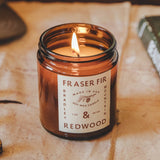 lit candle in amber colored jar labeled "fraser fir and redwood" 