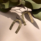 Close up of texture brass arch drop earrings