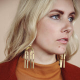 Model wearing bright brass "Joni" statement earrings comprised of modern brass shapes stacked and connected with jump rings creating a chandelier effect.