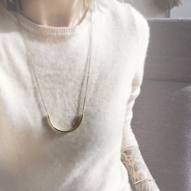 CIVAL Collective model in white sweater wearing long "Lydia" bright brass arc necklace on rolo chain.